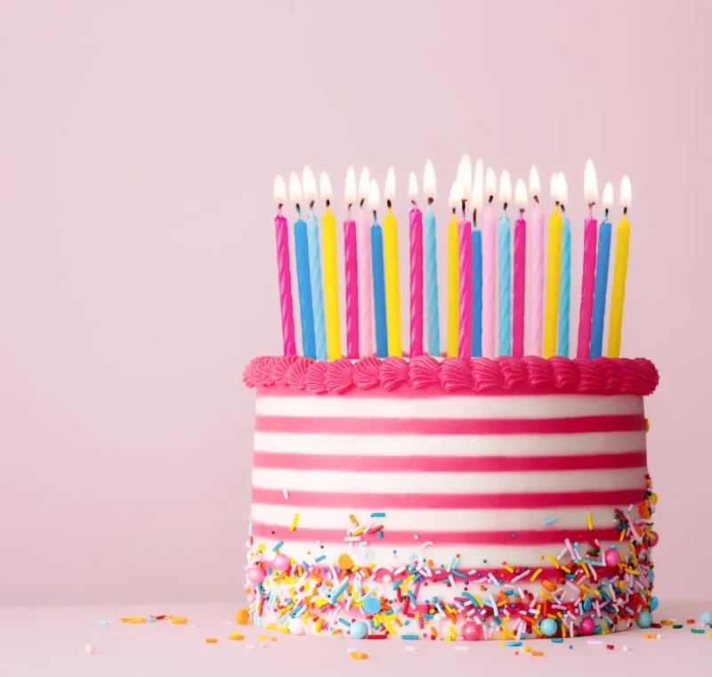 Pink and white striped birthday cake with lots of candles